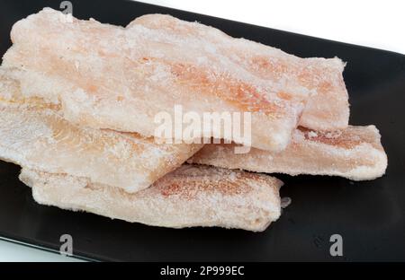 Poisson surgelé sur plaque noire, filet de morue blanc, filet de merlu glacé, viande de goberge surgelée sur fond de plaque sombre Banque D'Images
