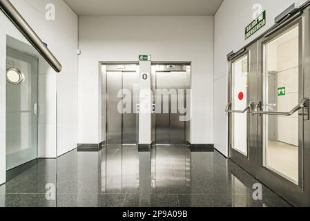 Couloir intérieur d'un immeuble de bureaux planchers en granit noir poli et portes d'accès en acier inoxydable pour deux ascenseurs Banque D'Images
