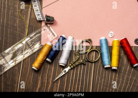 une vie de couture avec règle en plastique, mètre ruban, fils assortis, ciseaux vintage dorés sur table en bois brun Banque D'Images