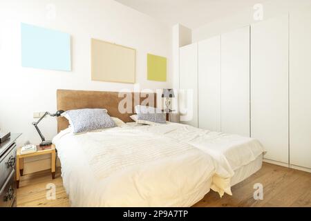 Chambre avec lits doubles, armoires en bois blanc, couvre-lits beige et tête de lit en velours brun clair Banque D'Images