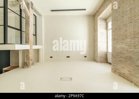 Chambre vide d'un appartement loft avec des murs en briques apparentes, d'autres murs blancs lisses et une chambre avec des cloisons en verre et du métal noir Banque D'Images