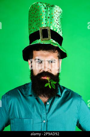 Patrick homme de la journée. Homme sérieux dans un chapeau vert avec trèfle dans la bouche. Homme barbu dans un chapeau vert. Tradition irlandaise. Le jour de la Patricks, le léopard barbu. Banque D'Images