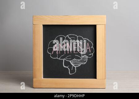 Petit tableau noir avec le cerveau dessiné et le mot Amnesia sur la table blanche en bois Banque D'Images
