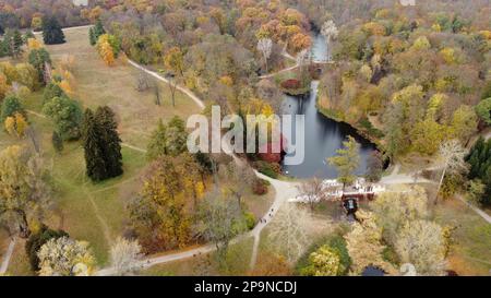 Magnifique vue sur le paysage du parc d'automne avec des lacs avec des cygnes, des arbres avec des feuilles vertes rouges jaunes, un pré, une architecture, une chute d'eau et des personnes marchant le long de chemins de terre le jour de l'automne. Arrière-plan naturel Banque D'Images