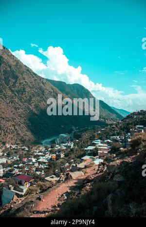 La vie au milieu des montagnes - une vue à vol d'oiseau des maisons nichées entre des sommets imposants, avec un ruisseau doux qui serpente à travers la vallée en contrebas. Banque D'Images