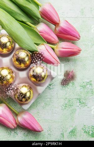 Porte-œufs de Pâques peint de couleurs dorées et tulipes roses sur fond de bois vert. Vue de dessus. Espace pour le texte. Banque D'Images