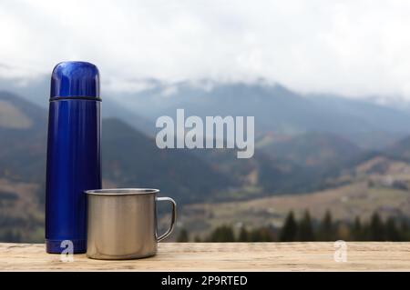 Thermos bleus et mug en métal sur une table en bois contre le paysage de montagne. Espace pour le texte Banque D'Images