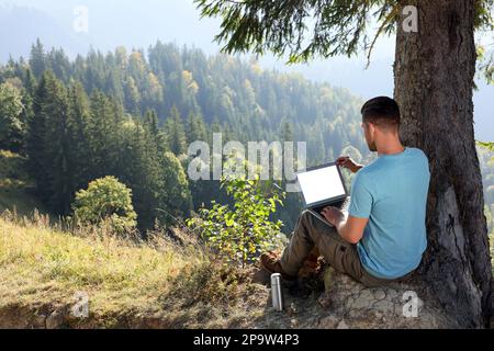Homme travaillant sur un ordinateur portable à l'extérieur entouré d'une belle nature, vue arrière Banque D'Images