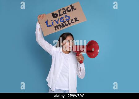 Une femme émotive criant dans le mégaphone tout en tenant le signe avec la phrase Black Lives Matter sur fond bleu clair. Mettre fin au racisme Banque D'Images