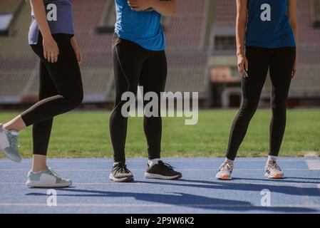 Trois coureurs se tenant sur une piste de sport bleue, par une journée ensoleillée Banque D'Images