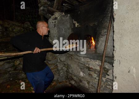 Staycation, homme senior cuisinant des pizzas au feu de bois dans un four en pierre extérieur traditionnel Banque D'Images