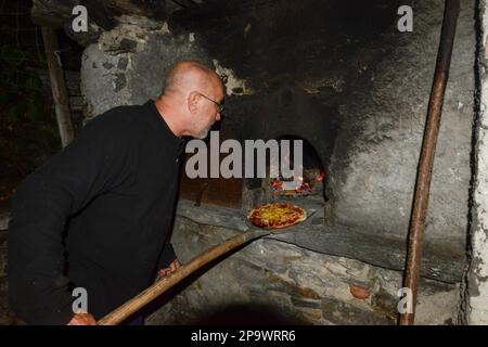Staycation, homme senior cuisinant des pizzas au feu de bois dans un four en pierre extérieur traditionnel Banque D'Images