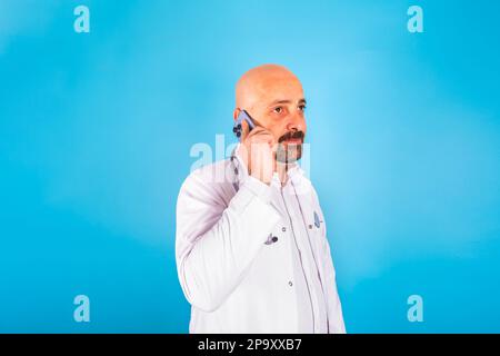 Un médecin caucasien parlant au téléphone. Sur fond bleu, espace de copie. Consulter un collègue, parler au patient. Médical. Banque D'Images
