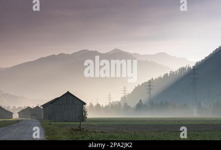 Vue sur la vallée de Praettigau, près de Klosters en Suisse, tôt le matin, avec champs de ferme et granges en bois, lignes électriques et montagnes Banque D'Images