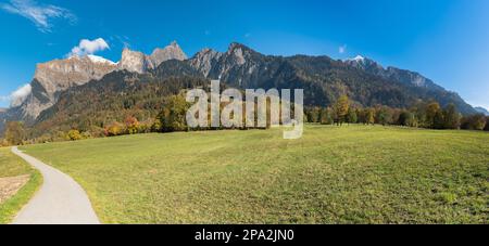 Paysage de montagne d'automne dans les Alpes suisses près de Maienfeld avec arbres de couleur d'automne et forêt et sommets enneigés de montagne avec une route de gravier et un pré dedans Banque D'Images