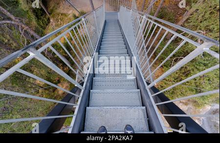 Escaliers métalliques menant à la forêt depuis une plate-forme d'observation avec des pieds mâles en chaussures bleues au premier plan dans le Surselva près de Flims en Suisse Banque D'Images