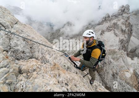 Un jeune homme beau grimpeur sur un front de roche raide et exposé grimpe une via Ferrata à Alta Badia dans le Tyrol du Sud Banque D'Images