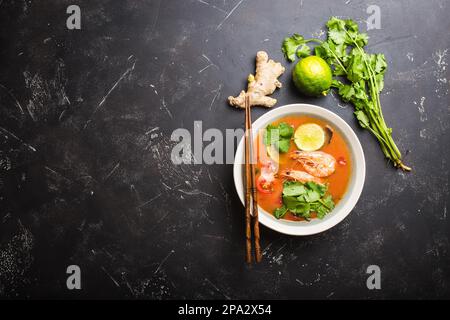 Soupe thaïlandaise traditionnelle épicée et chaude tom yum avec crevettes, citron vert, coriandre dans un bol sur fond de pierre rustique avec espace pour le texte, vue du dessus. Banque D'Images