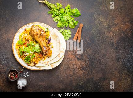 Une vue de dessus de poulet biryani avec riz basmati, légumes, coriandre et pain naan dans un bol, un plat traditionnel indien épicé, sur pierre rustique Banque D'Images