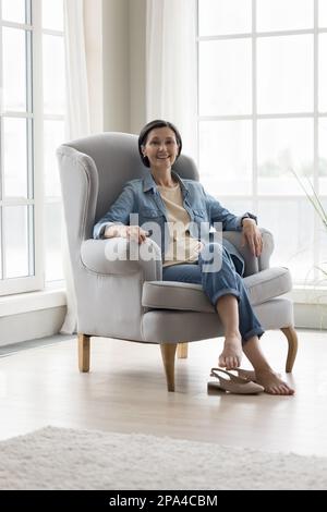 Bonne femme mature dans un fauteuil décontracté reposant dans un portrait à la maison Banque D'Images