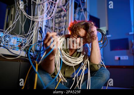 Un ingénieur informatique fou et fou enveloppé de fils et de câbles dans la salle des serveurs Banque D'Images