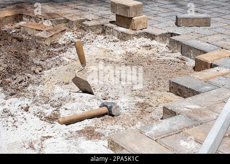 Une truelle dans le sable à côté d'un petit maillet et des blocs de béton par temps ensoleillé. Banque D'Images