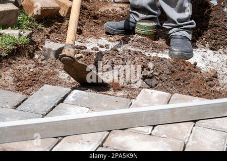 Brésilien utilisant une houe pour préparer le sol pour la pose de blocs de béton. Banque D'Images