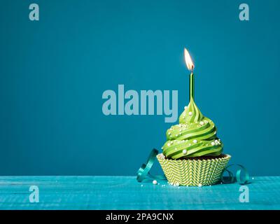 Gâteau d'anniversaire crème au beurre avec glaçage vert, bougie allumée, saupoudrer et ruban sur fond bleu sarcelle. Banque D'Images