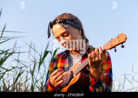 Femme guitare. Jeune fille marchant sur fond de nature. Petite fille dehors sur la prairie verte. Accord ukulele. L'été. Musiciens de gens. Sourire Banque D'Images