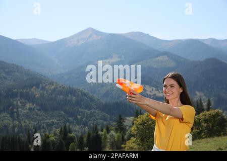 Bonne femme avec un pistolet à eau s'amusant dans les montagnes par beau temps Banque D'Images