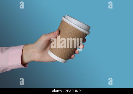 Femme tenant une tasse à café en papier à emporter sur fond bleu, gros plan Banque D'Images