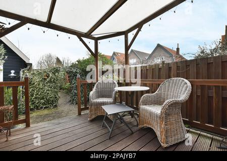 un espace extérieur avec des chaises et des tables sous un auvent blanc sur une terrasse en bois dans la photo est prise de derrière Banque D'Images