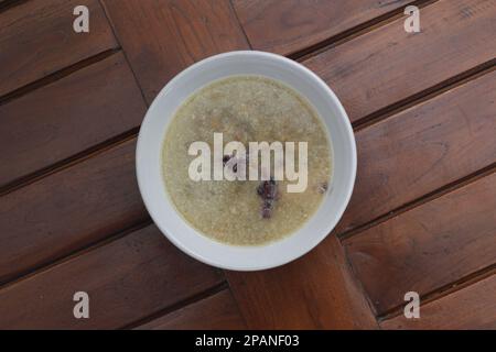 un gros plan d'un bol de porridge aux haricots verts et de riz noir collant surgit dans le lait de coco, servi chaud et prêt à manger sur un fond en bois avec un n Banque D'Images