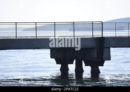 Ancien quai en béton recouvert d'intempéries avec garde-corps en métal perforé monté sur le côté. Banque D'Images
