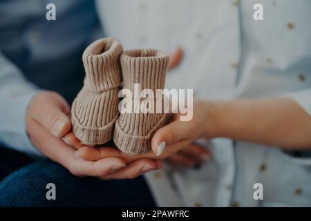 Plan court de futurs parents anticiper pour enfant tenir bébé bottes montrer de petites chaussures pour bébé à venir. Parentalité grossesse amour de naissance et conce de famille Banque D'Images