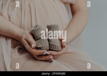 Concept de maternité et de grossesse. La mère expectative se prépare à donner naissance à l'enfant tient des bottes dans les mains pose à l'intérieur étant sur le troisième trimestre Banque D'Images