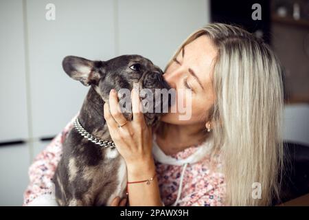 Femme blonde il adore et embrasse son bouledogue français dans un mignon museau. Entretien et soins des chiens. Animaux de compagnie sains. Banque D'Images