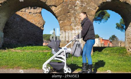 une jeune femme avec une poussette marche dans le parc, près de l'ancien mur romain, italie rome Banque D'Images