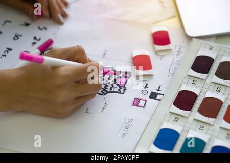 Gros plan mode designer main utiliser Magic stylo peinture sur le motif pour le tissu. Des échantillons de tissus aux couleurs vives sont disponibles sur l'établi. Banque D'Images