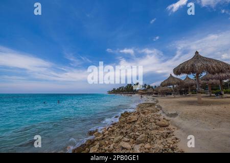 Vue sur l'océan Atlantique et la plage avec chaises longues et parasols sur fond ciel bleu avec nuages blancs. Aruba. Banque D'Images