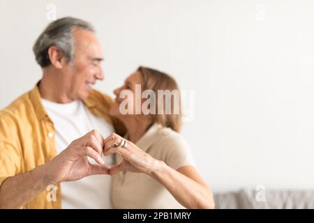 J'aime les couples séniors qui s'embrassent tout en faisant un geste de forme cardiaque avec les mains, en regardant les uns les autres et en souriant, espace libre Banque D'Images