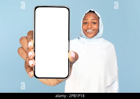Maquette d'application mobile. Femme islamique noire positive montrant un grand téléphone portable et démontrant un écran vide pour votre conception Banque D'Images