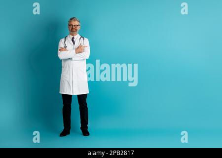 Joyeux médecin d'âge moyen avec les bras croisés posant sur le bleu Banque D'Images