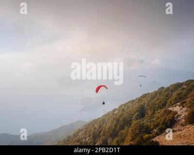 Parapente dans le ciel. Tandem de parapente volant au-dessus de la mer et des montagnes par jour nuageux. Vue sur le parapente et le lagon bleu à Oludeniz, Turquie. Sport extrême. Paysage Banque D'Images