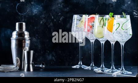 Ensemble de cocktails tonique gin. Boissons tendance avec citron vert, citron, pamplemousse, orange, concombre, soda et herbes épicées dans des verres à vin, fond noir Banque D'Images