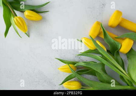 Des haltères de gym et des fleurs de tulipes en cadeau pour la fête des femmes, la fête des mères ou l'anniversaire. Entraînement physique sain, entraînement sportif plat avec espace de copie. Banque D'Images