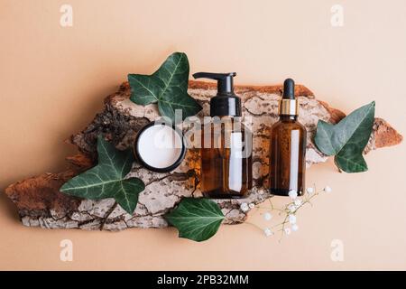 Lotion cosmétique, sérum et pot de crème en paquets vierges sur une écorce d'arbre avec des feuilles vertes. Cosmétiques naturels, spa et bien-être. Vue de dessus, plat l Banque D'Images