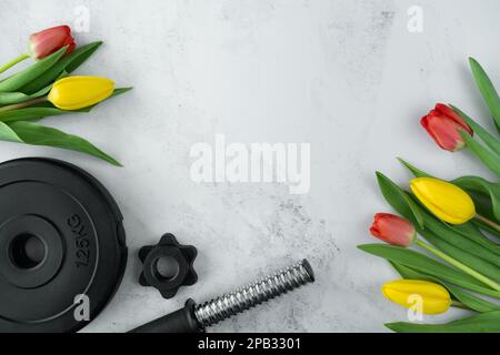 Gym haltères barbell plaque de musculation et tulipes fleurs. Cadeau pour la fête des femmes, la fête des mères ou l'anniversaire. Séance d'entraînement de fitness avec espace de copie. Banque D'Images