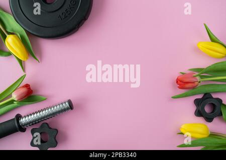 Gym haltères barbell plaque de musculation et tulipes fleurs. Cadeau pour la fête des femmes, la fête des mères ou l'anniversaire. Séance d'entraînement de fitness avec espace de copie. Banque D'Images