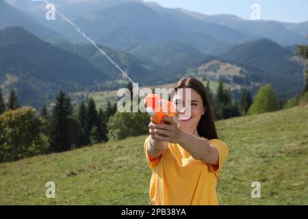 Bonne femme avec un pistolet à eau s'amusant dans les montagnes par beau temps Banque D'Images